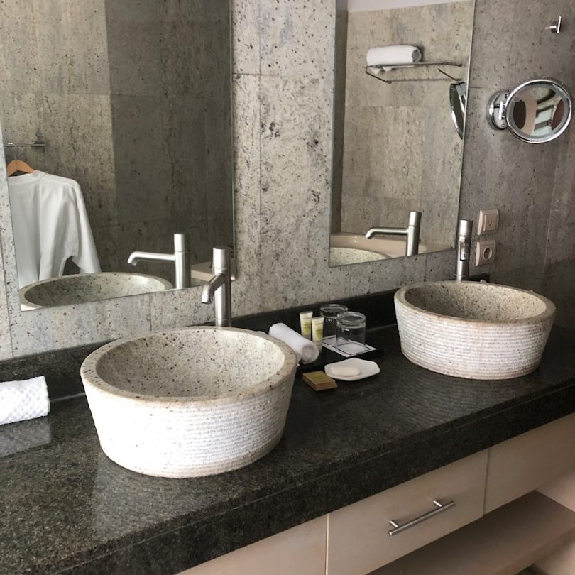 Zwei weiße Waschbecken auf einer dunklen Arbeitsplatte mit Spiegeln im Hintergrund.